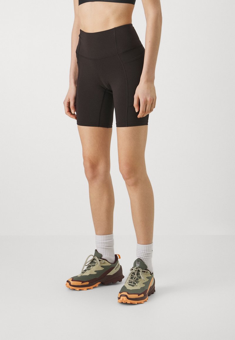 Schwarze, hoch taillierte Shorts mit einem eleganten Design. Sie verfügen über einen glatten Stoff und eine figurschmeichelnde Silhouette. Kombiniert mit olivgrünen und orangenen Sportschuhen.