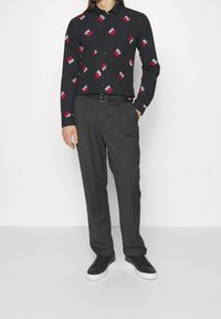 Czarna koszula z długim rękawem z czerwono-białym nadrukiem tekstu "HUGO", zestawiona z szarymi, dopasowanymi spodniami i czarnymi tenisówkami.