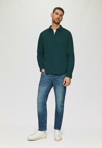 Donkergroene button-up overhemd met een kraag, gecombineerd met lichtblauwe jeans en witte sneakers, met een soepele textuur en een casual pasvorm.