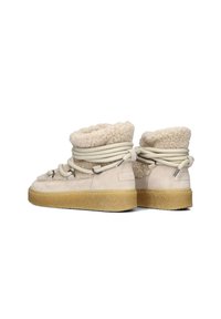 Beige suède enkellaarzen met een fluffy shearling voering, ronde veters en een gestructureerde rubberen zool. Voorzien van metalen accenten en stiksel details.