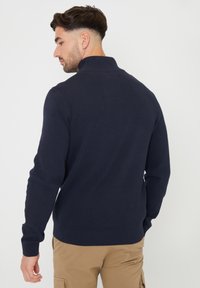 Tmavě modrý pletený svetr s vysokým límcem a dlouhými rukávy, s žebrovaným lemem a manžetami, vyrobený z měkkého, lehkého materiálu.