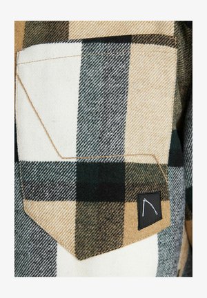 Gevlochten overhemd met tan, witte en groene ruiten, voorzien van een borstzak en een zwart labelpatch. Gemaakt van een zachte, gestructureerde stof.