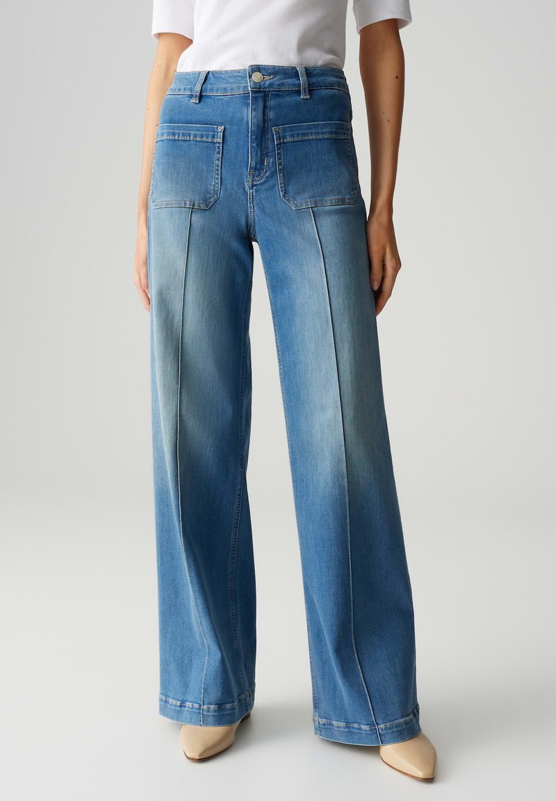 Jean large en denim bleu clair, avec une taille haute, des poches avant et une texture lisse, associés à des chaussures nude à bout pointu.