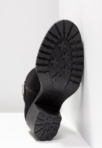Bottine en suède noir avec une semelle en caoutchouc texturée présentant un motif à crampons et une fermeture éclair latérale pour un accès facile.