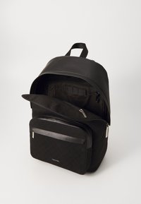 Svart ryggsäck gjord av texturerad tyg med en slät läderöverdel. Den har ett stort fack med dragkedja och en framficka med dragkedja.