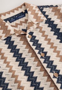 Kurzärmliges Hemd aus gewebtem Stoff mit Zickzackmuster in Creme, Braun und Marineblau. Mit Kragen und Knopfleiste. Insgesamt weiche Textur.