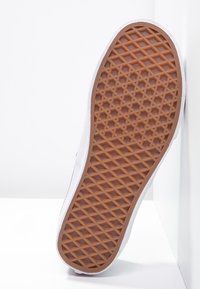 White sneaker sole with a textured, brown rubber outsole featuring a diamond pattern. The upper side is smooth and well-defined.