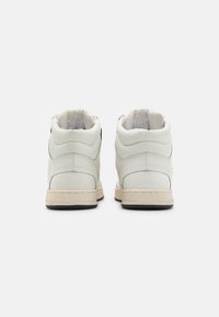 Sneakers alta bianche in pelle liscia, con accenti neri a contrasto, collare imbottito e suola in gomma con marchio 'GUESS'.