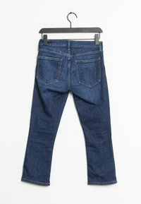 Jeans en denim bleu foncé suspendus à un cintre noir ; coupe droite avec cinq poches et accents de couture visibles sur les coutures.