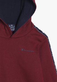 Felpa maroon con cappuccio blu navy e pannelli laterali a contrasto. Presenta un logo sul petto e una texture morbida, progettata per il comfort.