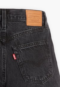 Bolsa trasera de unos jeans negros de Levi's, con etiqueta roja de Levi's y parche de cuero marrón con el logotipo de la marca encima del bolsillo.