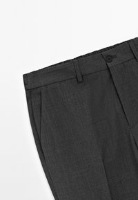 Pantaloni grigio carbone con frontale piatto, pieghe e vita con chiusura a bottone. Il tessuto presenta una trama strutturata.