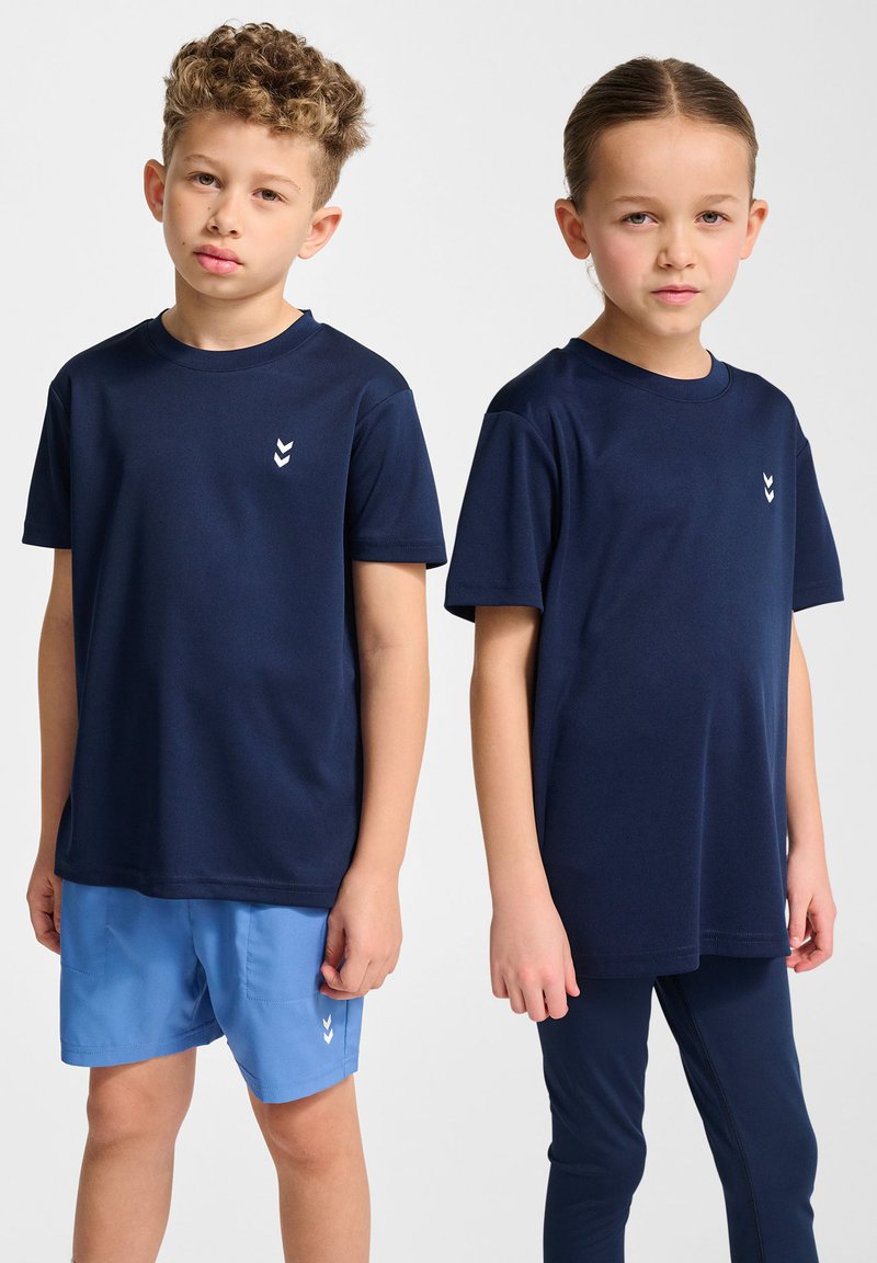 T-shirts de sport bleu marine exposés, avec des manches courtes et un petit logo blanc. Un modèle porte un short bleu ; l'autre porte des leggings bleu marine.