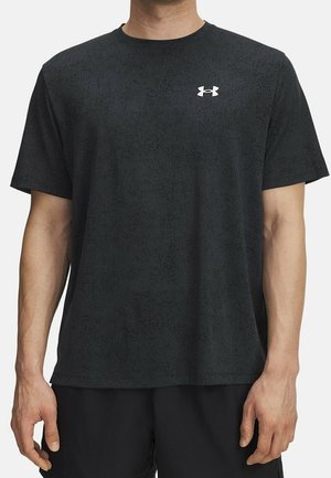 Mann trägt schlichtes dunkelgraues T-Shirt mit kurzen Ärmeln und kleinem weißem Under Armour-Logo auf der oberen Brust, kombiniert mit schwarzen Shorts.