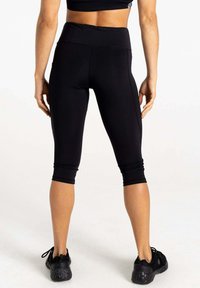 Schwarze Capri-Leggings aus dehnbarem Material, mit hohem Taillenbund und figurbetontem Schnitt, ergänzt durch schwarze Sportler-Schuhe.
