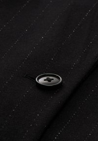 Zwarte stof met subtiele strepen en een fijne textuur, met een ronde zwarte knoop in het midden, vastgenaaid met een zwarte draad.