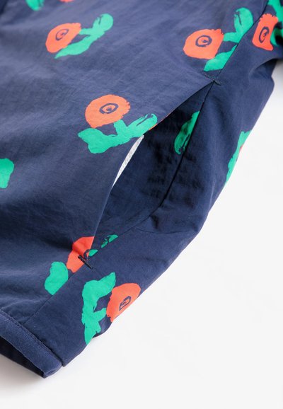 Tissu bleu marine avec imprimé floral orange et vert, doté d’une poche latérale avec coutures visibles et détails sur l’ourlet.