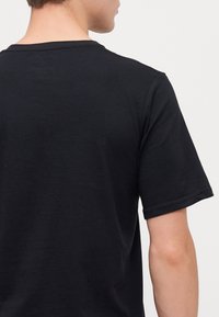 T-shirt noir à manches courtes avec un col rond. Le tissu semble doux avec une texture lisse, avec des coutures visibles à l'ourlet.