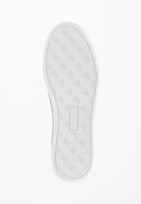 Semelle de basket en caoutchouc blanc présentant un motif en losange avec un logo en relief. Le bord est texturé pour une meilleure adhérence et durabilité.