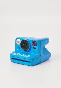 Blue analog camera with a rounded body, prominent lens, flash, and a slot for photos; features "MoMA" logo in bold lettering.
