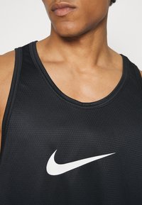 Top sin mangas negro de Nike con una textura de malla transpirable, escote redondeado y un prominente logo en forma de swoosh blanco en la parte delantera.