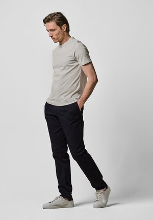 Grå kortærmet t-shirt parret med mørkeblå bukser og lyse sneakers. Materialet ser blødt ud, med en afslappet pasform og klassisk design.