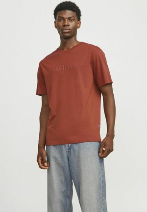 Kastanjefarvet bomulds T-shirt med korte ærmer, med prægede "ORIGINALS" tekst på brystet. Parret med løstsiddende lyseblå denim jeans.