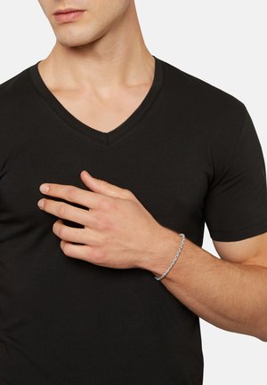 Silver chain bracelet on a hand; black V-neck T-shirt with smooth texture; focusing on the bracelet's details and style.