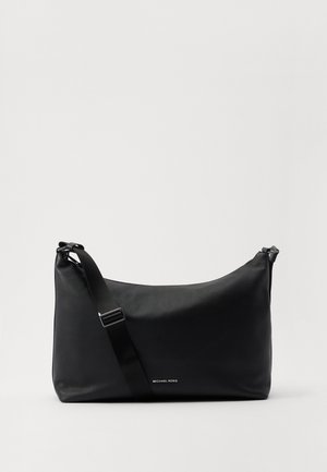 Sac bandoulière en cuir noir Michael Kors avec sangle ajustable et logo discret sur le devant, sur fond clair uni.