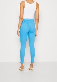 Jasnoniebieskie slim-fit dżinsy z pięcioma kieszeniami, wysokim stanem i przeszyciami. Modelka połączyła je z cielistymi szpilkami i białym topem na ramiączkach.