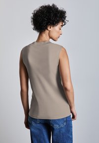 Top senza maniche di colore beige realizzato in morbido tessuto, con scollatura rotonda e una vestibilità comoda, abbinato a pantaloni in denim blu.