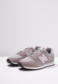 Szare sneakersy z połączeniem zamszu i siateczki, z białym logo, sznurowadłami, teksturowanymi detalami oraz czarną gumową podeszwą.