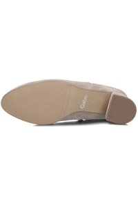 Beige suède dames schoen met een lage blokhak en een gestructureerde rubberen zool. Heeft een merkeen logo op de zool en een slank, afgerond te ontwerp.