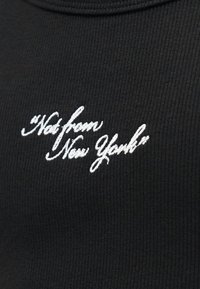 Czarny prążkowany materiał z białym kursywnym haftem z napisem „Not from New York” umieszczonym na środku klatki piersiowej.