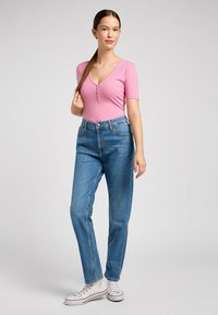 Lyserød ribbet bodysuit med korte ærmer og V-hals, parret med højtaljede blå lige ben jeans og hvide sneakers.