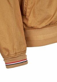 Braune Bomberjacke mit einem gerippten Bündchen in Rot, Weiß und Schwarz; aus glattem, leichtem Stoff mit einem Reißverschluss gefertigt.