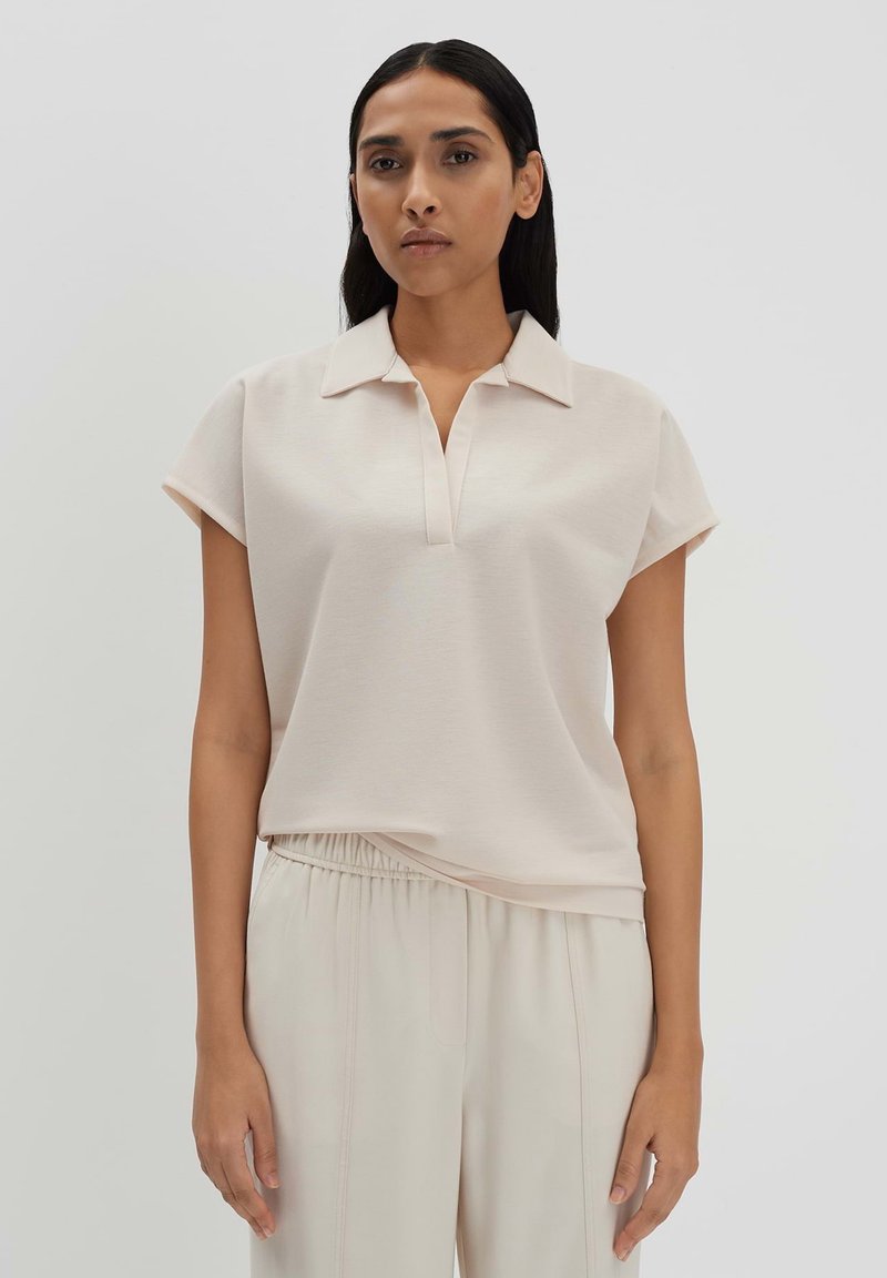 Hellrosa Poloshirt mit kurzen Ärmeln, Kragen und lockerer Passform, aus weichem Material gefertigt, kombiniert mit passenden hellen Hosen.