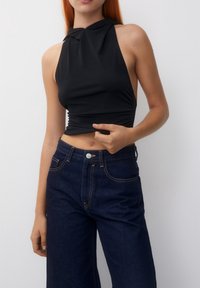 Un haut noir à bretelles avec un design noué au cou, fabriqué en tissu extensible, associé à un jean en denim sombre taille haute avec un bouton à l'avant.