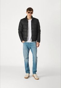 Svart vadderad jacka med hög krage, bärs över en vit t-shirt, i kombination med ljusblå denimjeans och vita sneakers. Solglasögon fulländar looken.