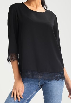 Blouse noire à manches trois-quarts, avec une bordure en dentelle aux poignets et à l'ourlet. Tissu lisse avec un col rond et une coupe décontractée.
