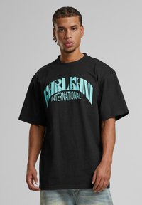 Black cotton t-shirt featuring a large turquoise "KARL KANI INTERNATIONAL" graphic in a bold, stylized font on the front.