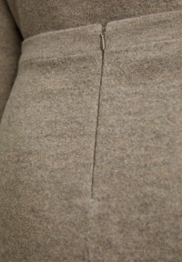 Vêtement en laine brun clair avec une texture lisse, doté d'une fermeture éclair sur le côté et de finitions de couture soignées.