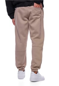 Beige sweatpants lavet af blødt materiale, med en baglomme, t�ætsiddende manchetter og en glat tekstur, parret med hvide sneakers.