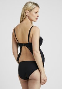 Top da bagno in stile tankini nero con dettagli in pizzo, spalline regolabili e design a schiena bassa, abbinato a slip bikini neri. Tessuto lisci.