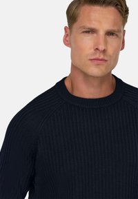 Marineblauwe geribbelde gebreide trui met een ronde halslijn en raglanmouwen, met een gevarieerde afwerking voor extra diepte.