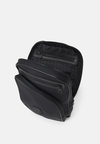 Borsa nera con zip, dotata di molteplici scomparti, esterno liscio, dettagli del logo e fodera interna testurizzata. Design leggero e compatto.
