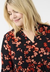 Vestido negro con flores que presenta flores rojas y melocotón, con un escote en V y una tela texturizada. El diseño acampanado añade suavidad al dobladillo.