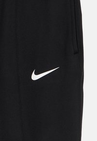 Μαύρο ύφασμα με λευκό λογότυπο Nike swoosh και ορατές ραφές κατά μήκος της πλευράς και της άκρης της τσέπης.