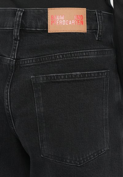 Black denim jeans with a square back pocket and a brown label featuring "BAUM UND PFERDGARTEN" embossed in pink. Distressed texture details visible.