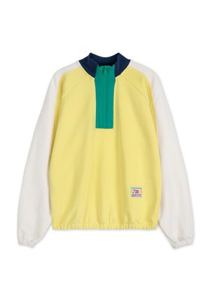 Žltý pulóver s bielymi rukávmi, modrým golierom a zeleným polozipsom. Má elastický lem a logo nášivku v dolnom ľavom rohu.